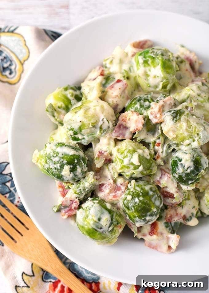 Creamy Bacon Brussels Sprouts on a white plate next to a wooden fork