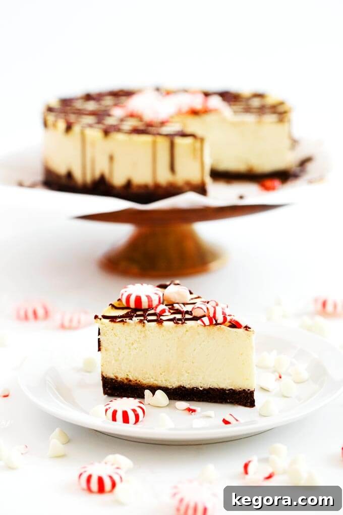 Slice of White Chocolate Peppermint on a white plate in front of rest of cheesecake on a cake stand 