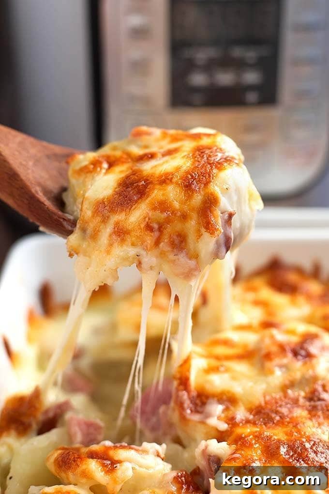 Wooden spoon serving Scalloped Potatoes from a white baking dish in front of a pressure cooker