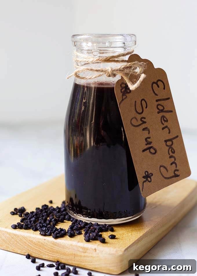 Small bottle of Elderberry Syrup with tap tied with twine on a wooden board with dried elderberries