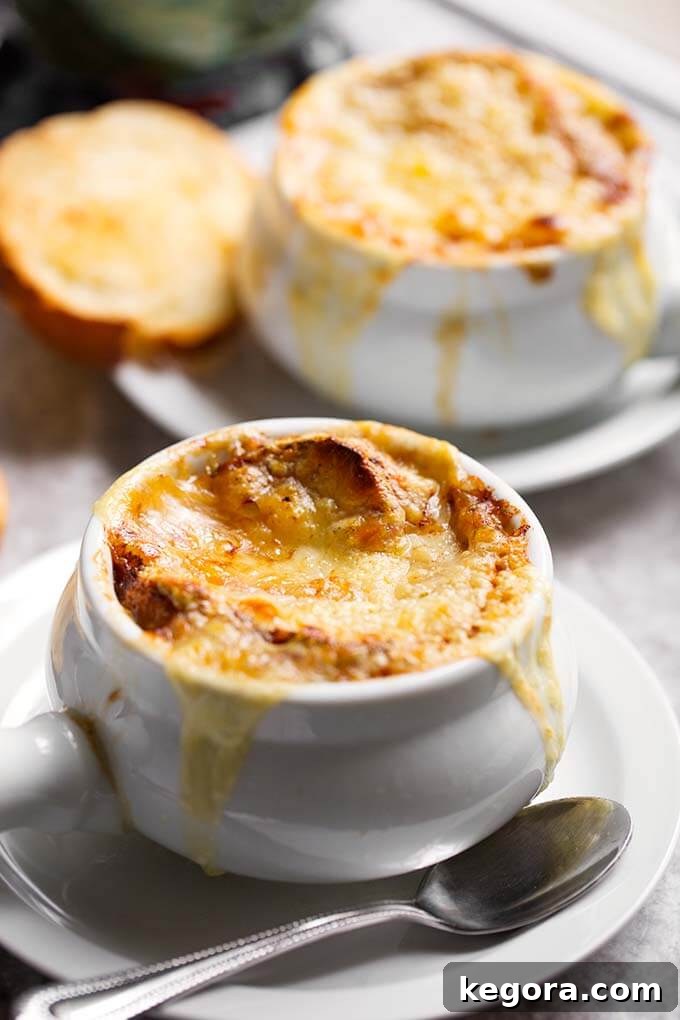 Two white bowls of French Onion Soup, topped with golden melted cheese and toasted bread, presented on white plates.