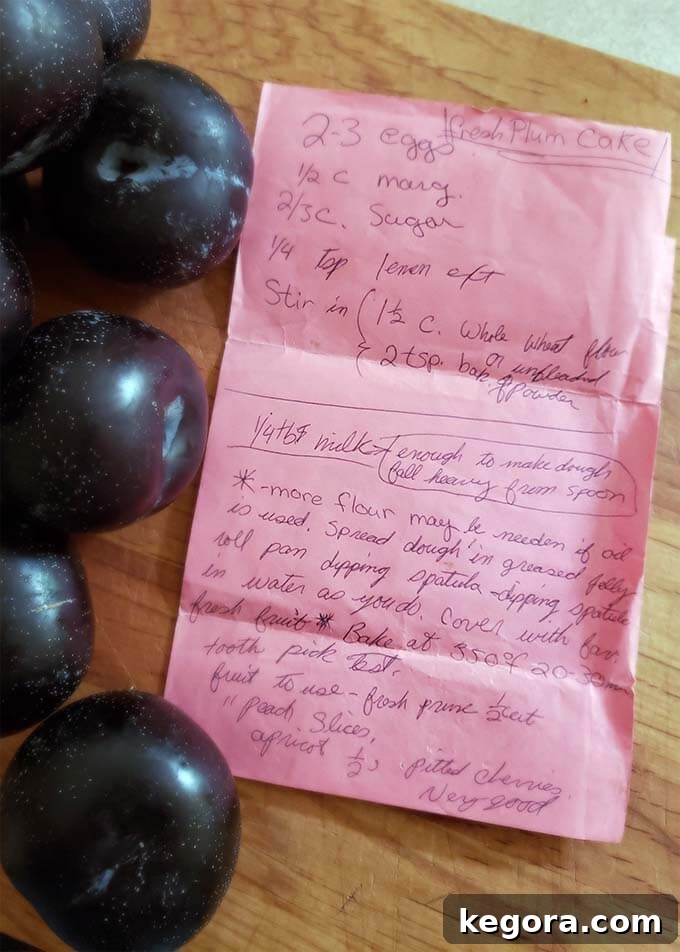 Several fresh plums and pink paper with recipe on a wooden board