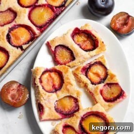 Four slices of Fresh Plum Cake, also called Pflaumenkuchen and Zwetschgenkuchen (German Plum Cake) on a white oblong plate next to baking sheet with remaining dish