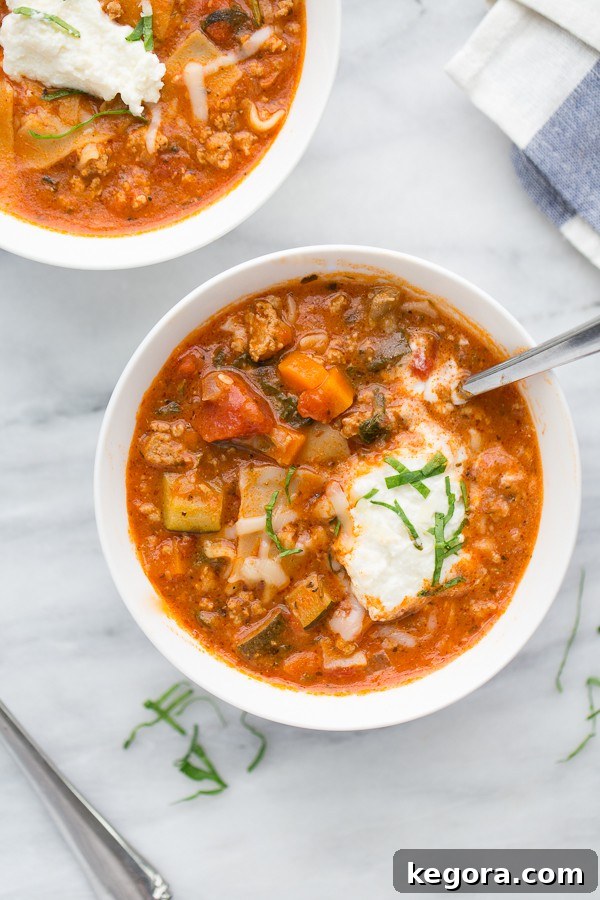 A vibrant bowl of Instant Pot Turkey Vegetable Lasagna Soup, garnished with fresh herbs and a dollop of creamy ricotta. The rich red soup is visible with pieces of lasagna noodles, ground turkey, and colorful vegetables.