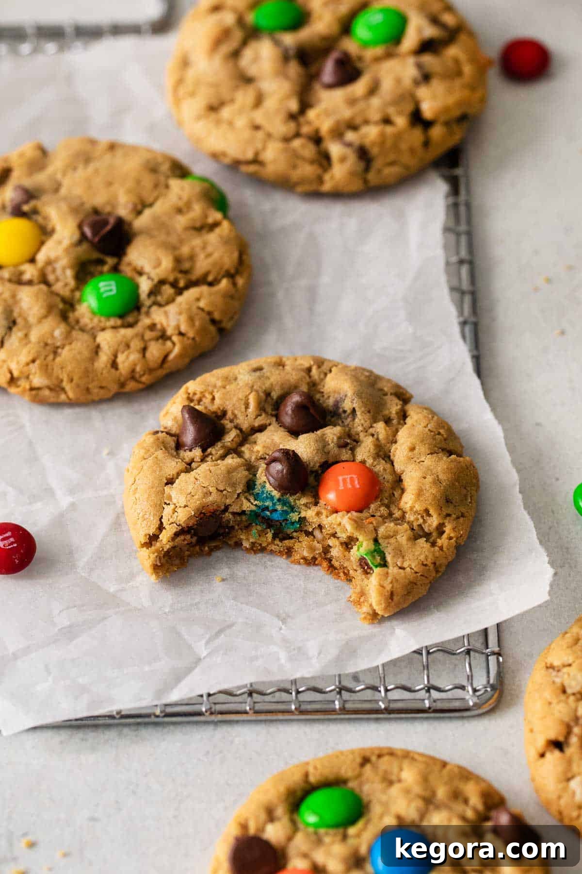 Monster Cookies Gluten-free monster cookies cooling on a wire rack, with one cookie having a bite taken out to reveal its soft, chewy interior.