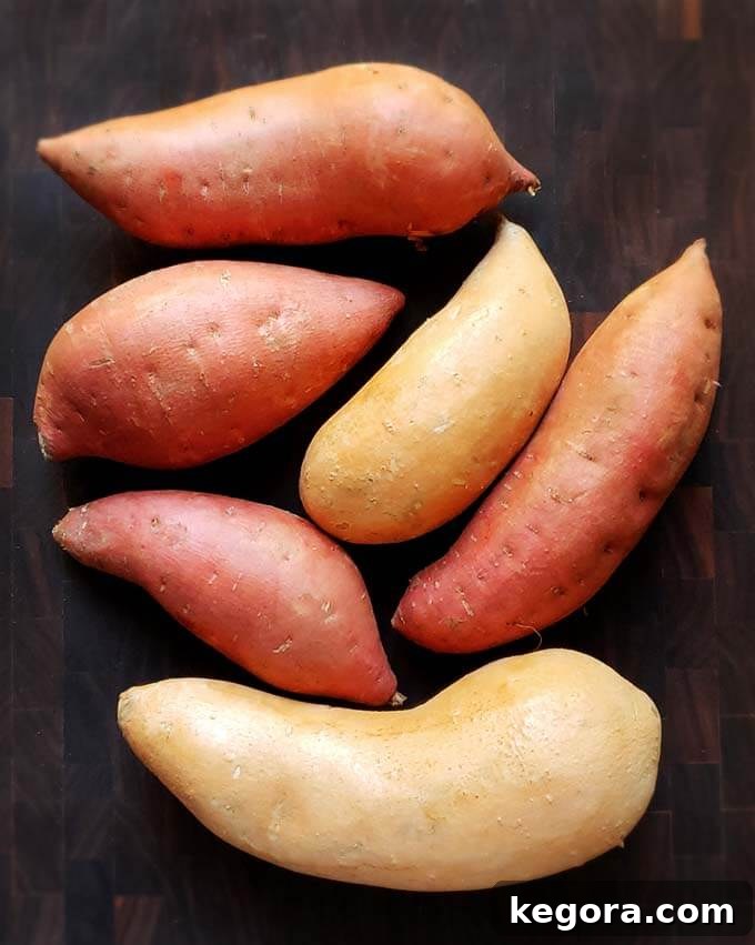 Six uncooked sweet potatoes on a dark wooden surface, showcasing various sizes and colors