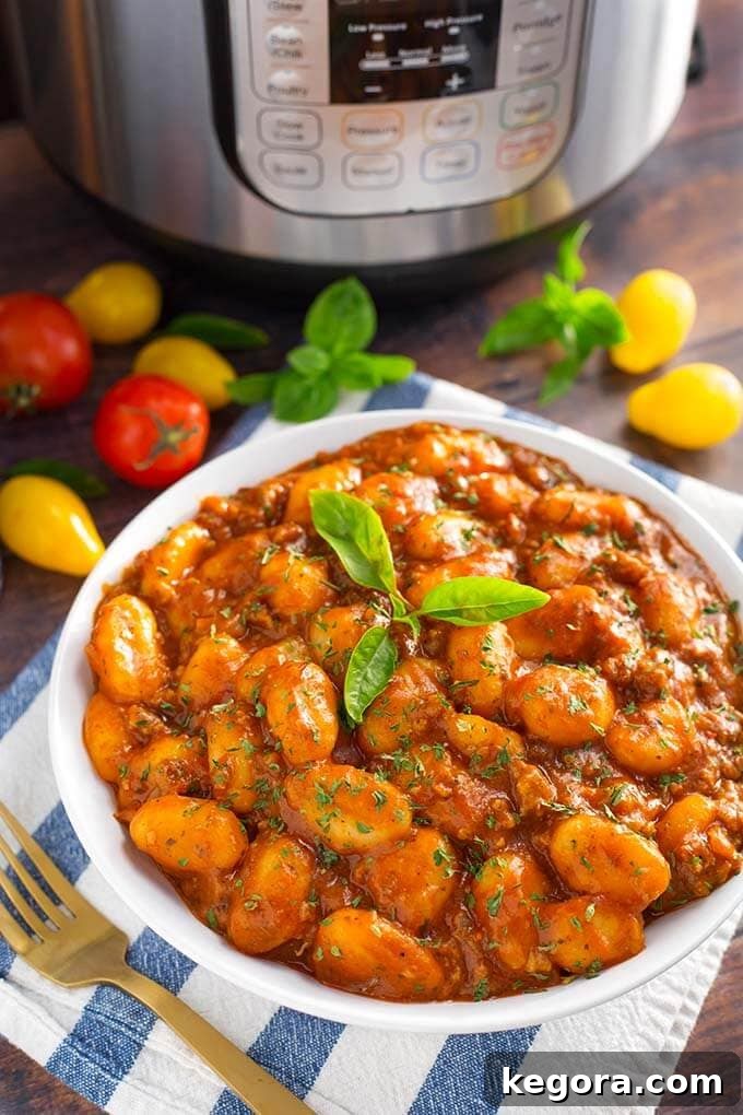 Sausage Gnocchi topped with fresh basil in a white bowl on a blue and white stripped napkin in front of a pressure cooker