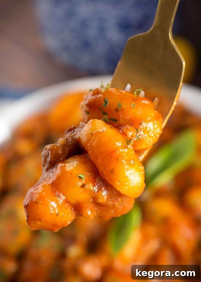 Hearty Instant Pot Sausage Gnocchi 3 Closeup of a fork holding Sausage Gnocchi over white bowl of Sausage Gnocchi