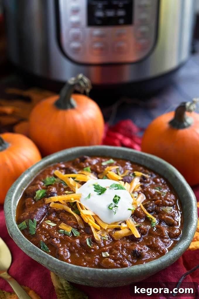 Cozy Instant Pot Pumpkin Chili 4 Pumpkin Chili topped with shredded cheese and sour cream in a turquoise bowl in front of a pressure cooker