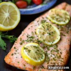 Beautifully baked Steelhead Trout Fillet garnished with fresh lemon slices and green herbs, highlighting its rich color and tender texture.