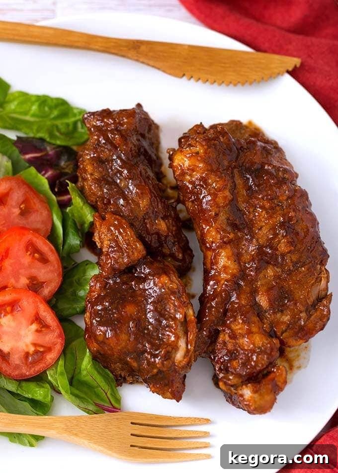 Instant Pot Country Style Ribs on a white plate with green beans and mashed potatoes, ready to be served with a wooden fork and knife.