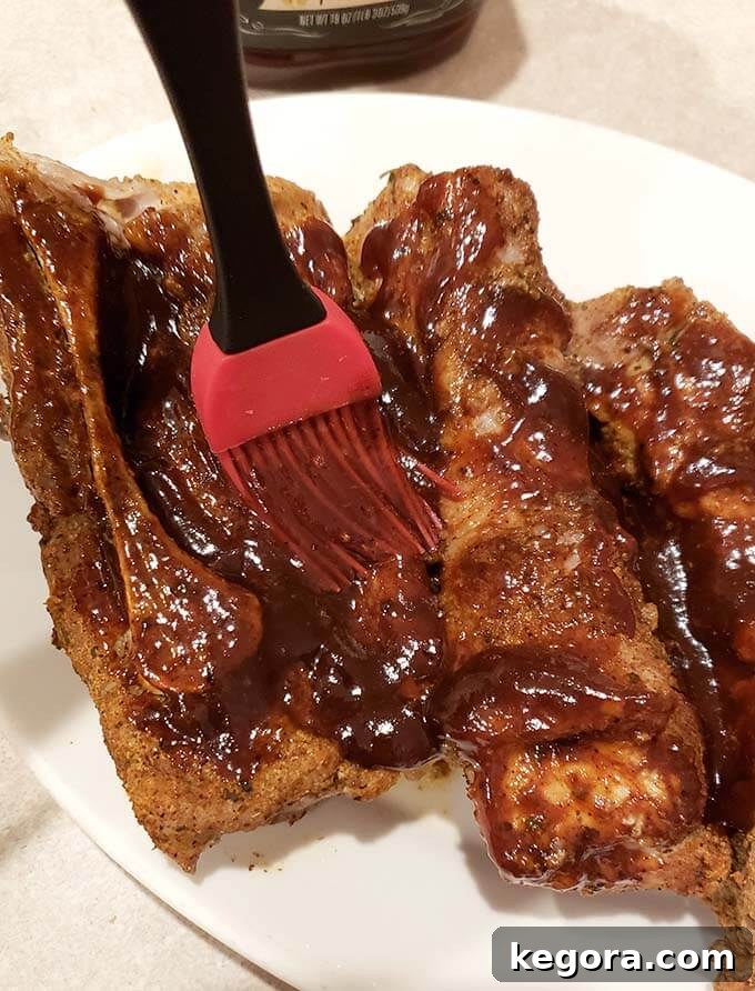 Red basting brush applying barbecue sauce onto juicy Instant Pot Country Style Ribs on a white serving plate, enhancing their flavor and appearance.