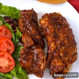 Two perfectly cooked Instant Pot Country Style Ribs on a white plate, garnished with fresh herbs and served with a side of vegetables.