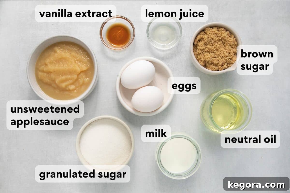 Various wet ingredients and sugars for applesauce bread, measured and laid out in separate bowls with labels for unsweetened applesauce, neutral oil, milk, eggs, vanilla extract, lemon juice, granulated sugar, and brown sugar.