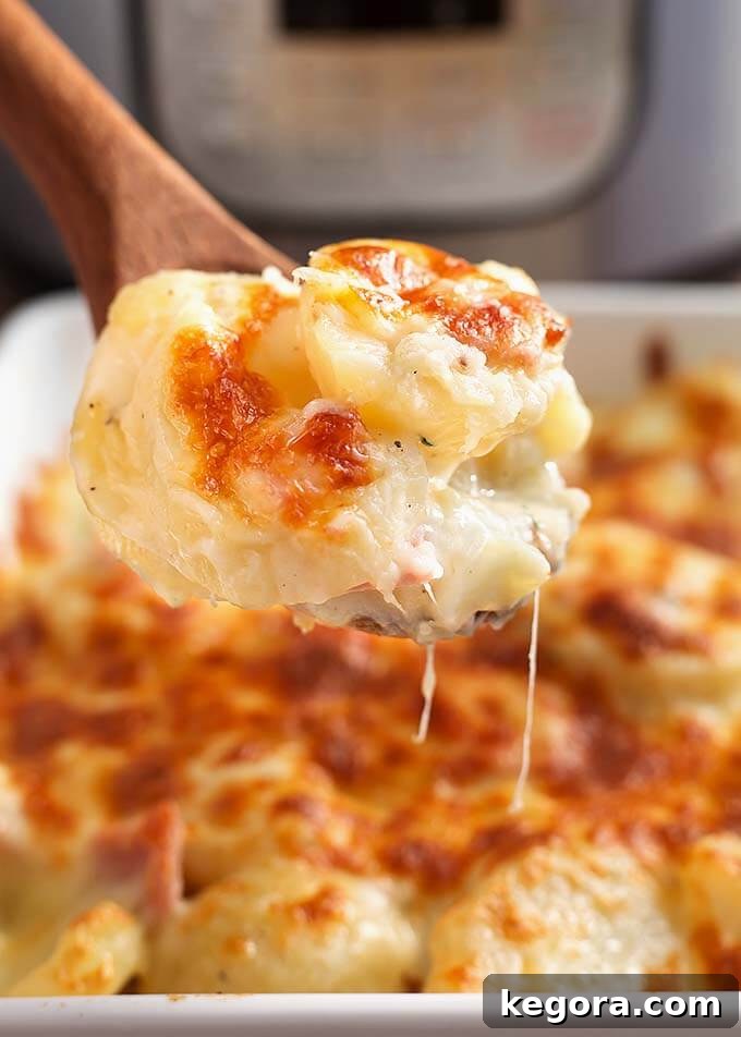 Close-up of a wooden spoon scooping golden-crusted Instant Pot Scalloped Potatoes from a white baking dish