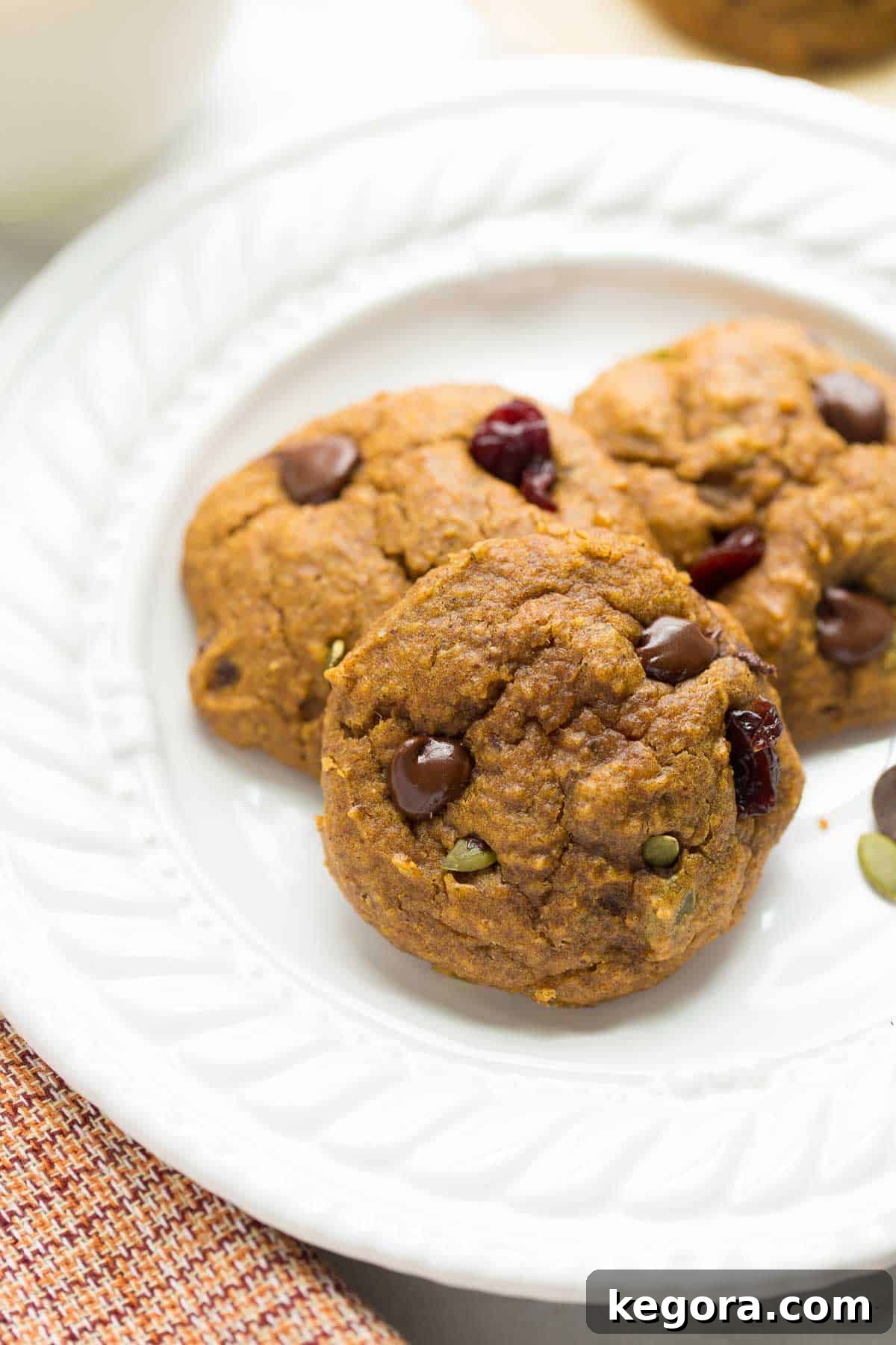 Cozy Vegan Pumpkin Breakfast Cookies 3 Close-up shot of three delicious vegan pumpkin cookies on a white plate with a festive plaid red and orange napkin, highlighting their inviting texture and appearance.