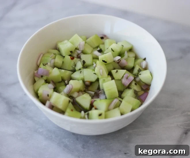 A crisp, vibrant bowl of chopped pickled cucumbers, fresh mint, and red pepper flakes, ready to refresh the palate