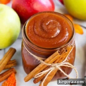 Small glass jar of Apple Butter with cinnamon sticks tied with twine in front of green and red apples and more cinnamon sticks