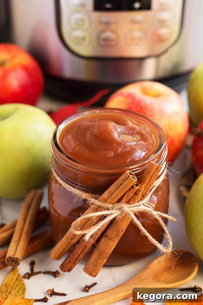 Quick Homemade Instant Pot Apple Butter 8 Small glass jar of Apple Butter with cinnamon sticks tied with twine in front of green and red apples and a pressure cooker
