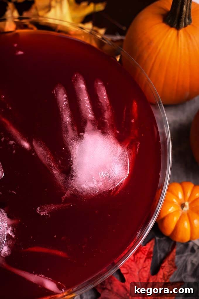 Ghastly Gala Punch 3 Closeup of ice hand floating in Spooky Halloween Party Punch in a glass punch bowl, adding a creepy element to the Halloween drink.