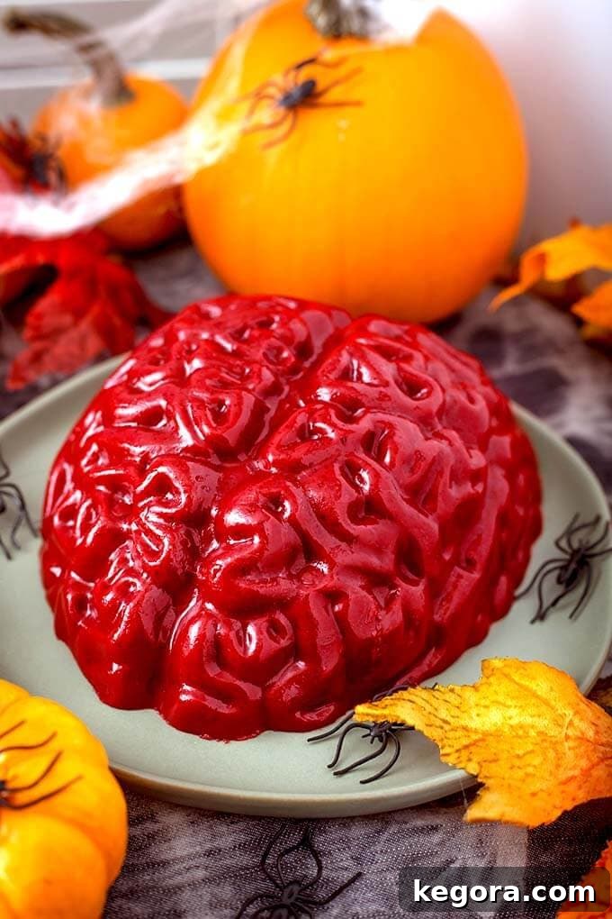 Ghoulish Jello Brain Recipe 11 A perfectly unmolded Halloween Jello Brain on a green plate, decorated with plastic spiders and a small pumpkin.