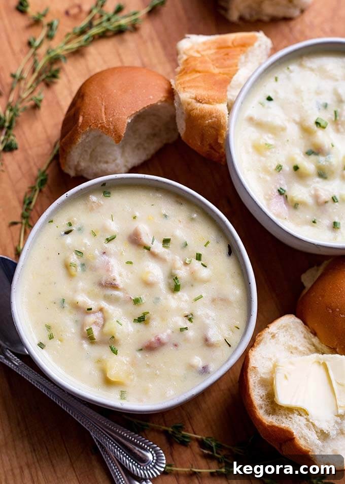 15 Delicious Instant Pot Soups 13 Two white bowls of creamy Instant Pot Clam Chowder, accompanied by crusty rolls on a wooden board, highlighting its award-winning, delicious, and easy preparation.