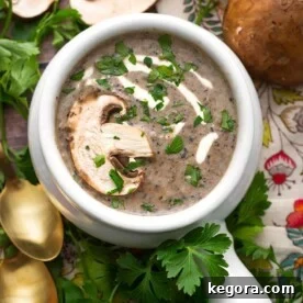 Top view of Creamy Instant Pot Mushroom Soup in a white handled bowl topped with a fresh mushroom slice and parsley garnish