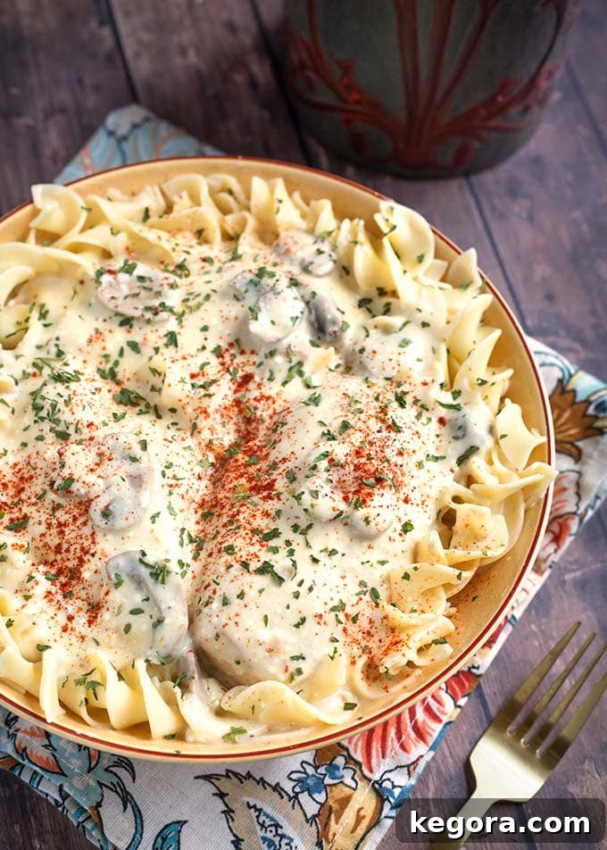 Creamy Chicken Breasts topping noodles in a beige bowl on top of a floral napkin, showcasing the rich texture and appealing presentation of the dish.