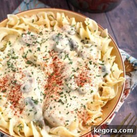 Creamy Chicken Breasts topping noodles in a beige bowl on top of a floral napkin, a delicious slow cooker meal.