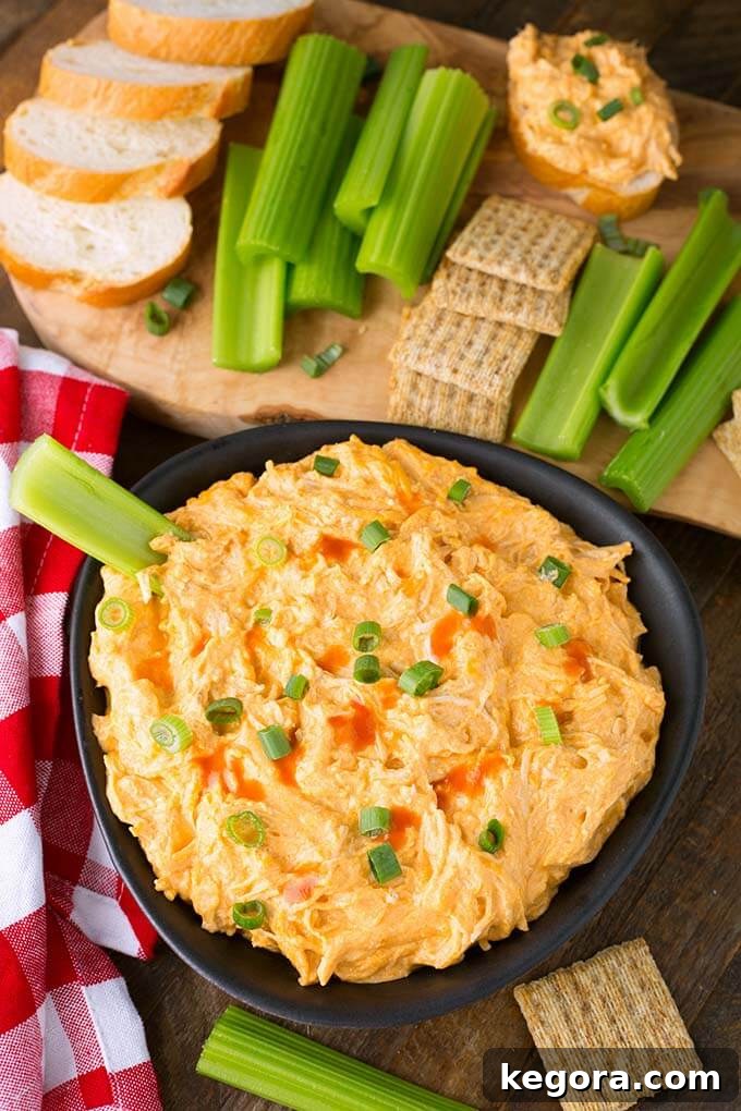 Creamy Crockpot Buffalo Chicken Delight 3 Top view of Slow Cooker Buffalo Chicken Dip in a black bowl, surrounded by fresh cilantro, various crackers, and slices of artisan bread on a wooden board