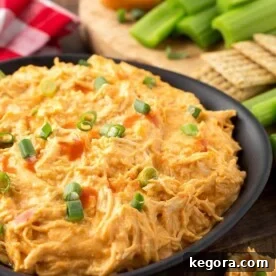 Buffalo Chicken Dip in a black bowl in front of a wooden board with crackers and celery