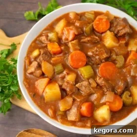 Beef Stew in a white bowl on a wooden board next to fresh parsley