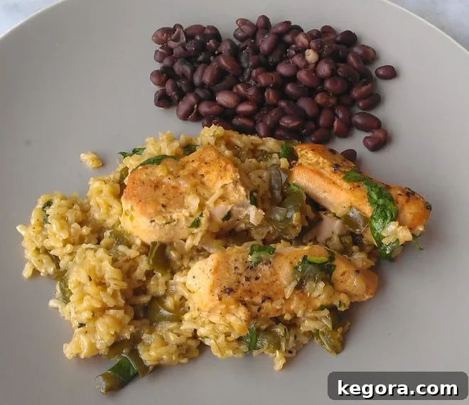 Skillet chicken over green rice with black beans on the side, served on a grey plate