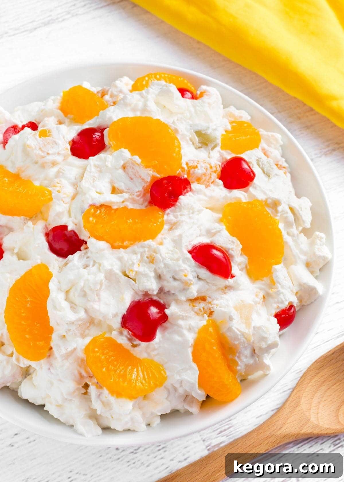Creamy Fruit Salad in white bowl, yellow linen, wood spoon
