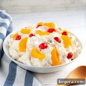Creamy Fruit Salad in a white bowl with wood spoon and striped napkin.