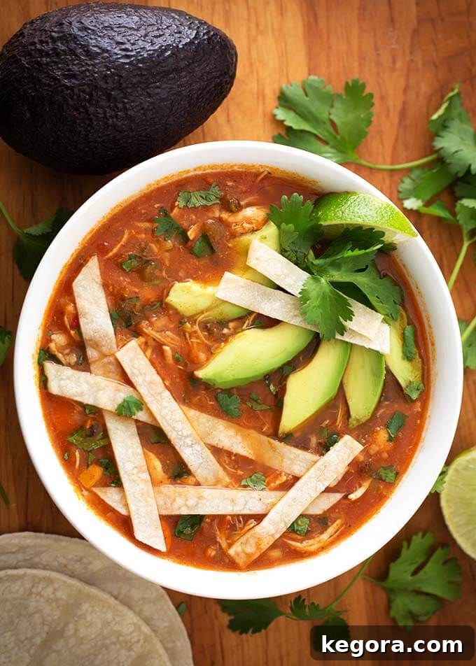 A steaming bowl of Instant Pot Chicken Tortilla Soup, garnished with crispy tortilla strips, fresh cilantro, and creamy avocado slices, resting on a rustic wooden board.