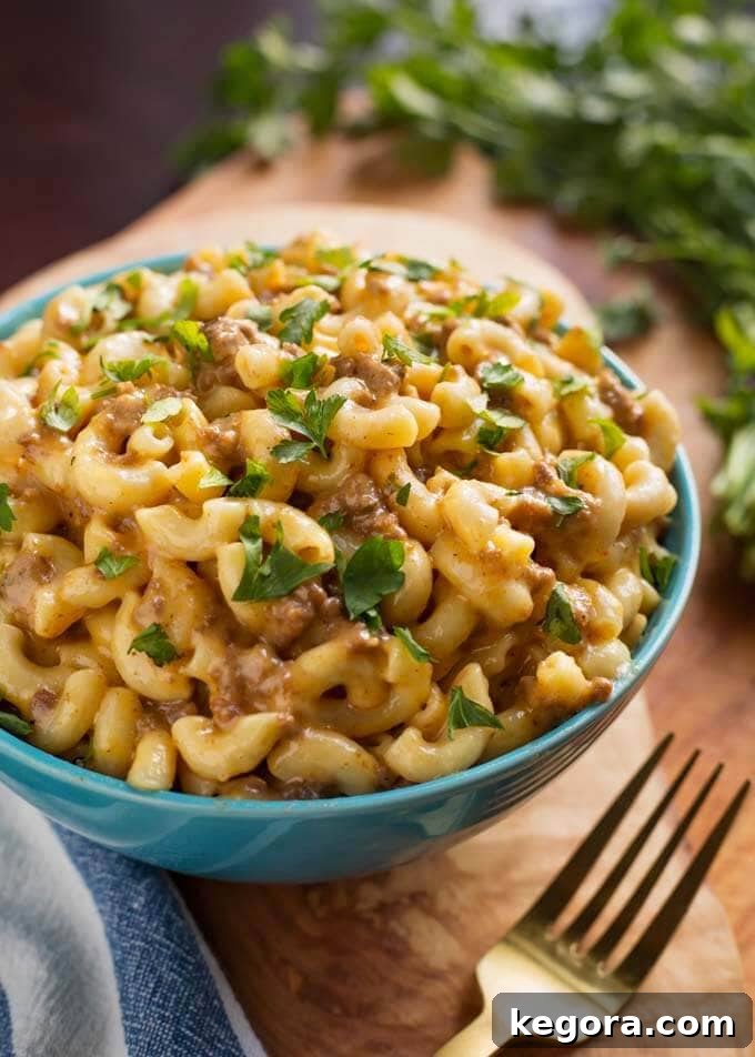 One Pot Cheeseburger Macaroni Magic 3 Cheeseburger Macaroni in a blue bowl next to a gold fork all on a wooden board