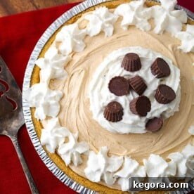 Easy Creamy Peanut Butter Pie 7 A vibrant image of a No Bake Peanut Butter Pie, sumptuously topped with whipped cream and various chocolate candies, highlights its irresistible appeal. This easy 5-ingredient pie delivers complex flavors, making it seem like a day-long project. It's the ultimate sweet and creamy dessert for all peanut butter enthusiasts, ideal for any event, from potlucks to parties, or just a simple, yummy treat.