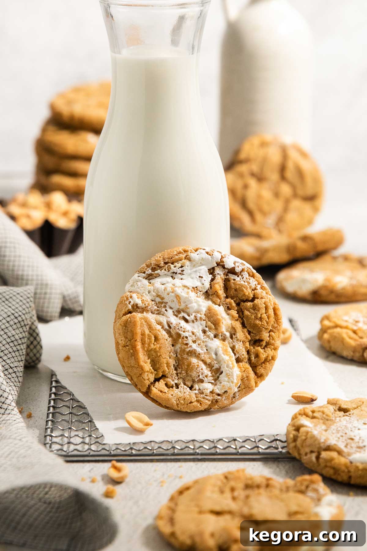 Gluten-Free Fluffernutter Cookies: Peanut Butter and Marshmallow 2 A glass bottle of milk sits on a wire rack with a peanut butter cookie filled with marshmallow cream leaning against it. More cookies and a napkin are scattered around in the background.