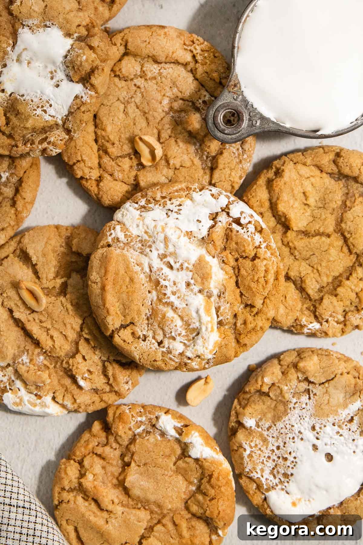 Gluten-Free Fluffernutter Cookies: Peanut Butter and Marshmallow 7 A close-up of several peanut butter cookies with marshmallow swirls, some topped with peanuts. A metal cup filled with milk is partially visible in the top right corner.
