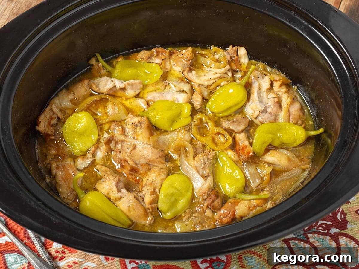 Crockpot Mississippi Chicken with pepperoncini peppers and onions in slow cooker.