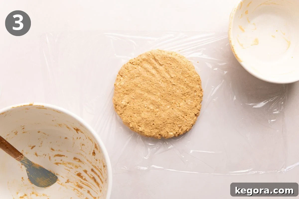 Flaky Gluten-Free Pumpkin Scones Recipe 6 Round disc of dough on plastic wrap, surrounded by two empty mixing bowls—one with a spatula and some dough remnants.