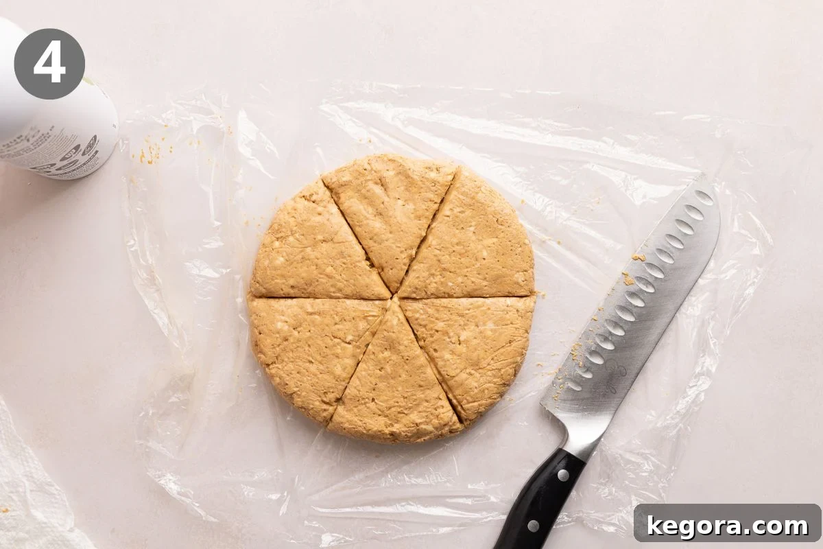 Flaky Gluten-Free Pumpkin Scones Recipe 7 A round disk of dough on plastic wrap is cut into six wedges with a large knife beside it.