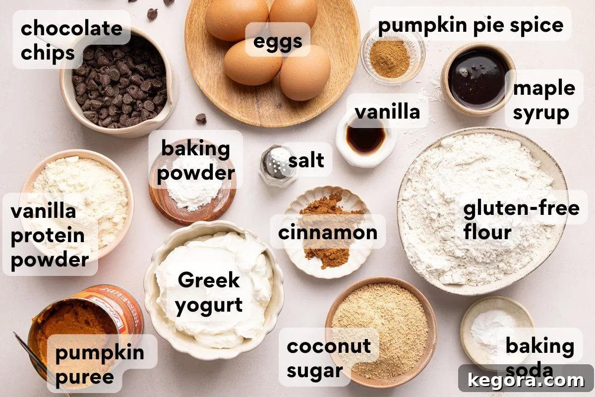 A variety of labeled baking ingredients are arranged on a counter, including eggs, chocolate chips, pumpkin puree, Greek yogurt, flours, spices, sweeteners, and baking powder and soda.